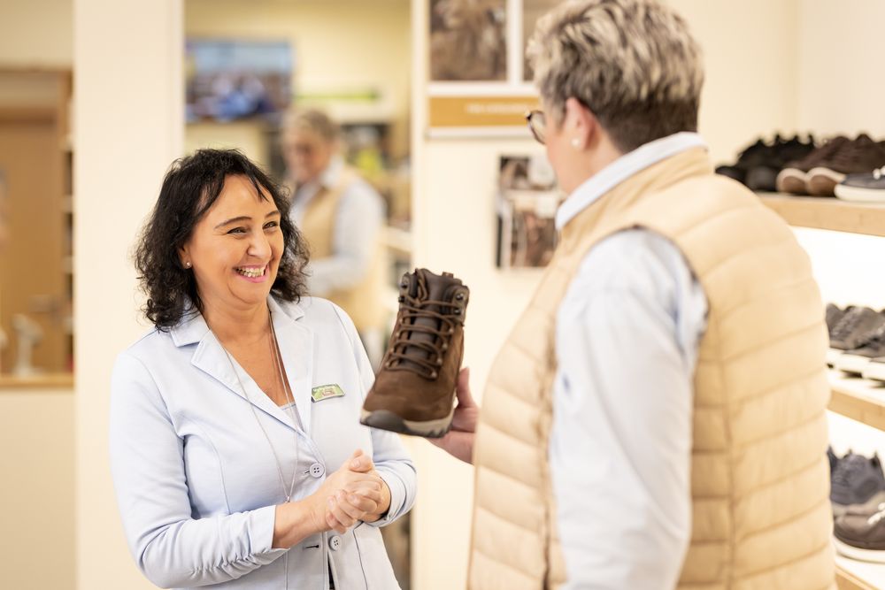 Mitarbeiterin reicht einer Kundin im Beratungsgespräch einen braunen Stiefel